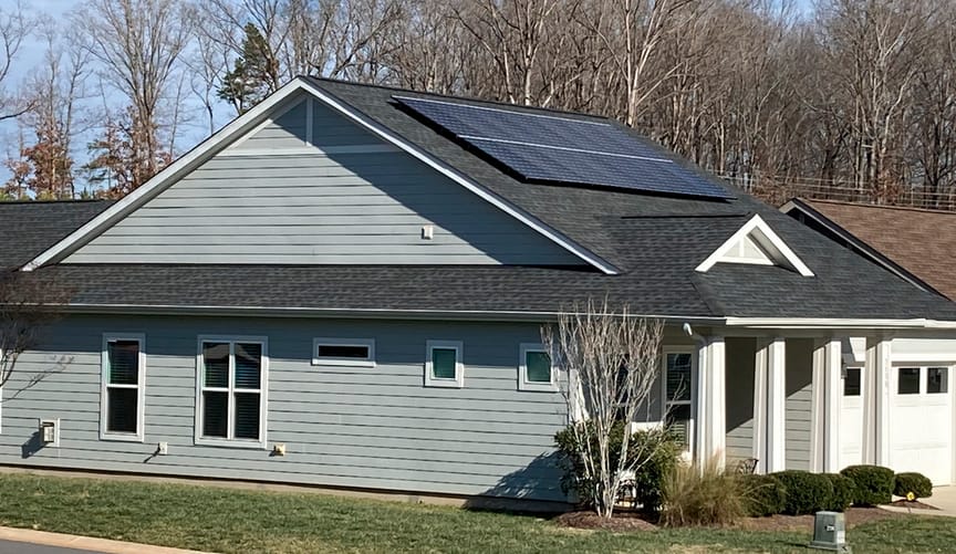 A gray, wood-paneled home with white columns and solar panels on its roof