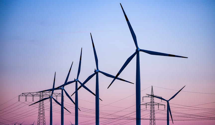 A row of wind turbines and transmission lines set against a sunset