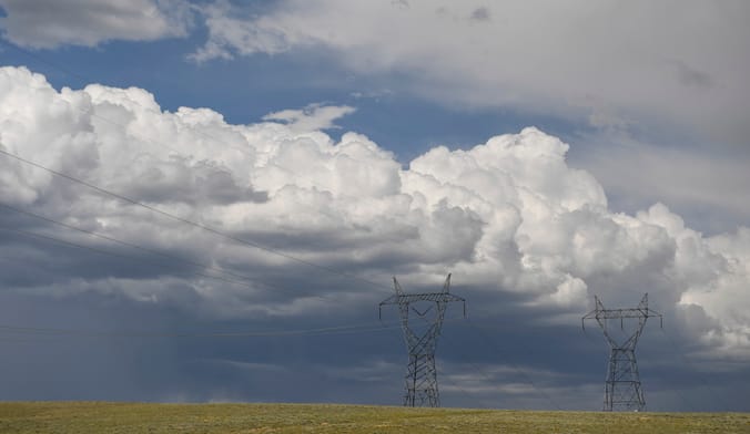 Two transmission towers and power lines under a cloudy sky on a large open plain
