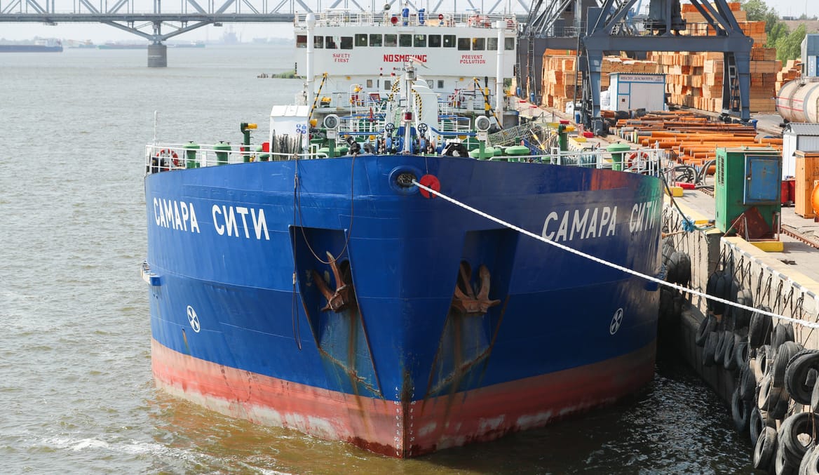 A large blue ship sits at port in a river