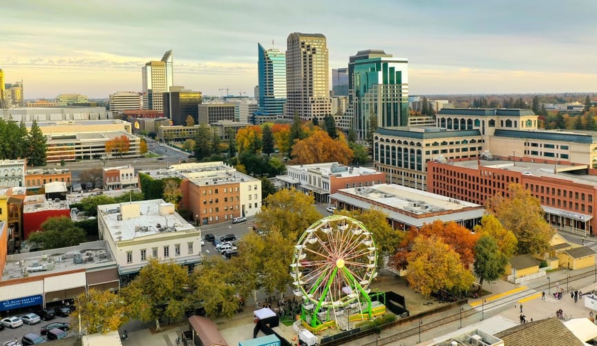 The skyline of sacramento with tall buildings in the background and a green ferris wheel in the foreground