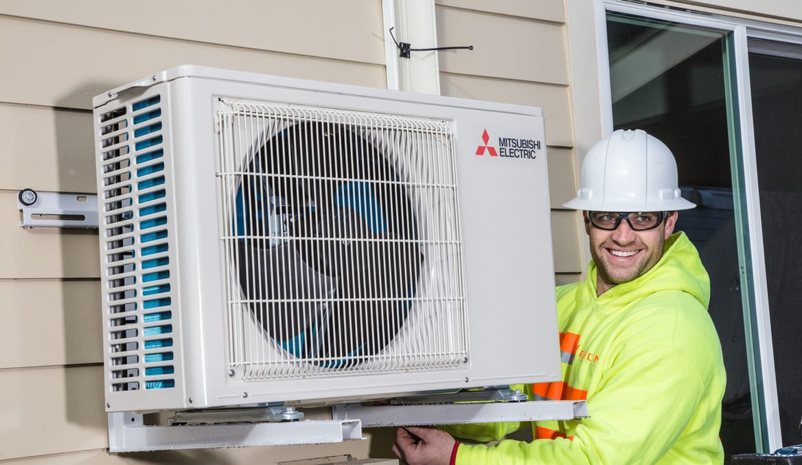 a man in safety gear and a neon vest smiles while installing a heat pump