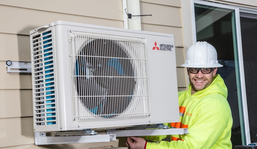 a man in safety gear and a neon vest smiles while installing a heat pump