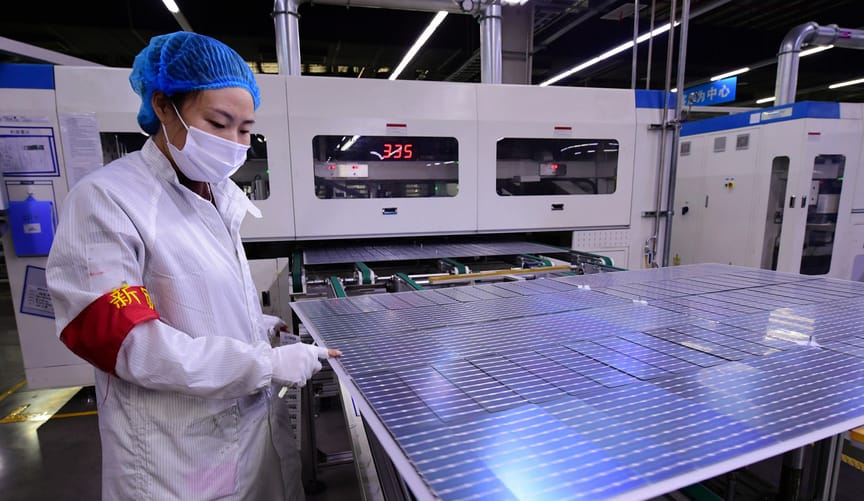 A factory worker wearing a mask and safety apparel points at a solar panel