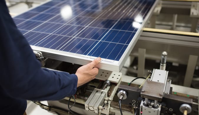 A worker in a blue shirt handles a solar panel in a factory