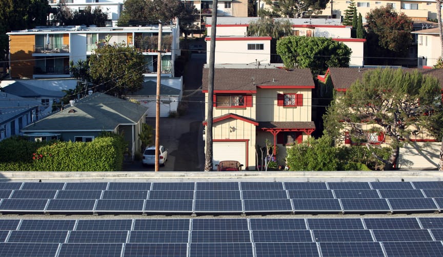 A condo with solar panels on its roof in the foreground. In the background are other houses on a residential street