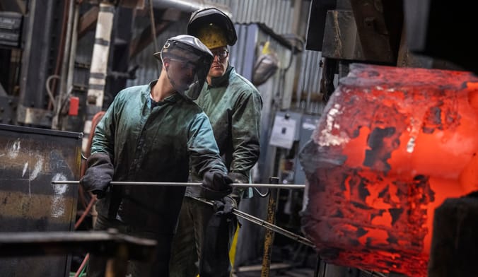 Two steelworkers work in front of a hot smelter