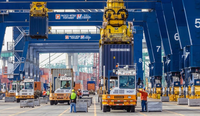 Dockworkers in safety gear move cargo containers at an industrial facility