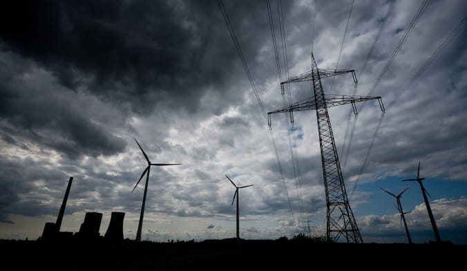 A coal plant with transmission lines and wind turbines underneath a gloomy twilight sky