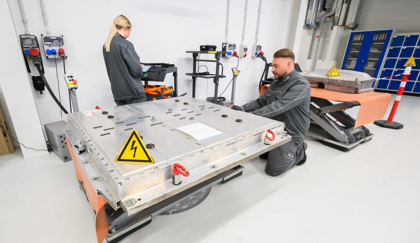 a male employee and a female employee perform tests on a large silver square used EV battery