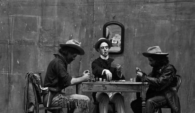 three cowboys are shown in an old black-and-white photograph playing poker