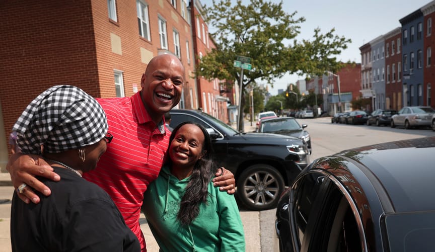 An African American man smiles and poses with two women on a city street