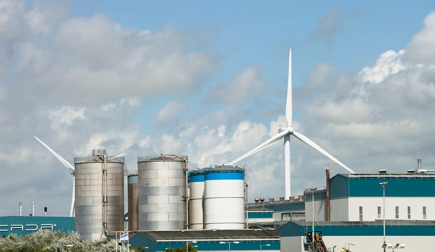 A large wind turbine is located in front a factory