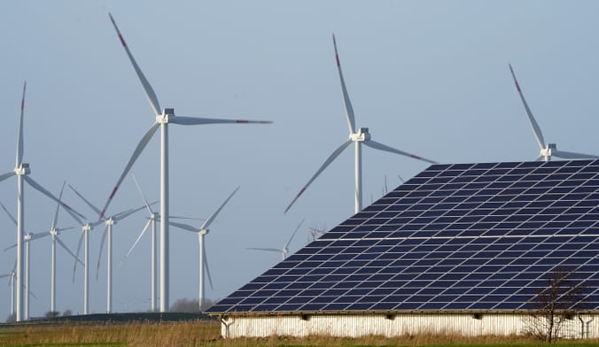 Spinning wind turbines and a solar array are shown next to each other in an open field