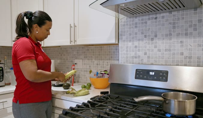 A woman in a red shirt with a ponytail peels a banana next to a gas stove