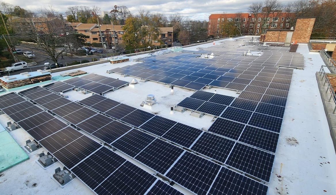 A large solar array on the roof of a multistory apartment building in a city