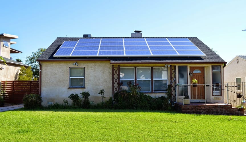 a small beige house with solar panels on the roof and a green grass lawn