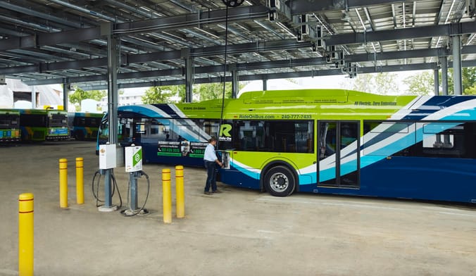 An employee plugs in an electric transit bus in a large industrial facility