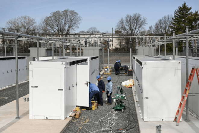 Utility workers work between rows of white cabinets at a utility substation