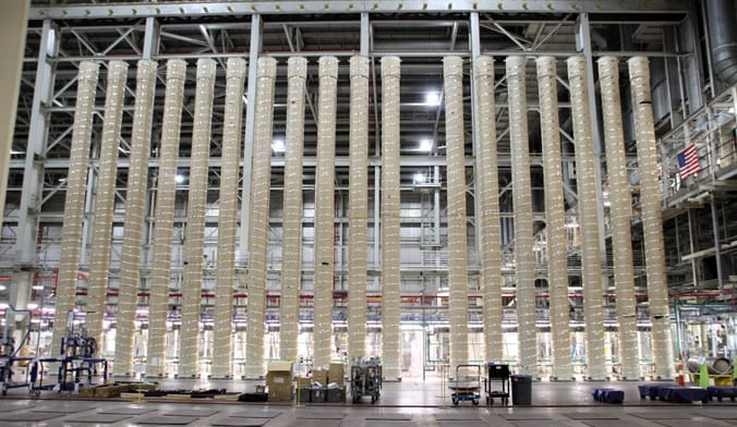 A row of very tall beige cylinders in a vertical row inside a large industrial facility
