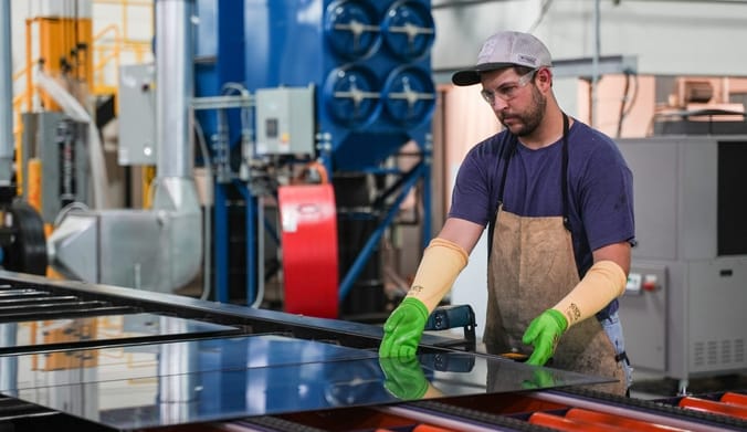 An employee in safety attire manipulates a large glass panel on a manufacturing line