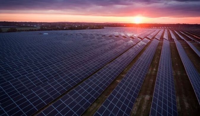 A large solar farm against the backdrop of a pink sunset