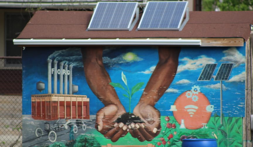 A colorful mural on a small solar-powered shed that shows two hands holding soil and a seedling
