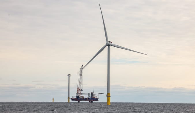 An operational wind turbine, along with two under construction behind it, and a lifting barge