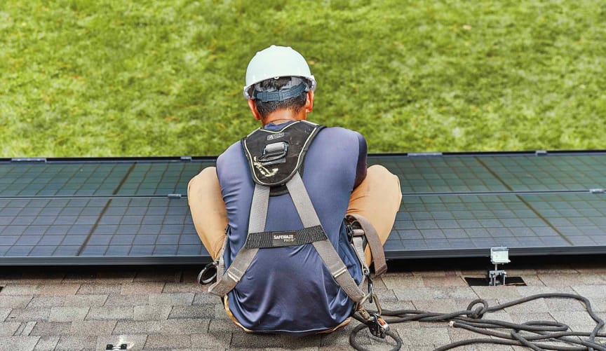 A worker in a hard hat and safety gear installing a rooftop solar panel