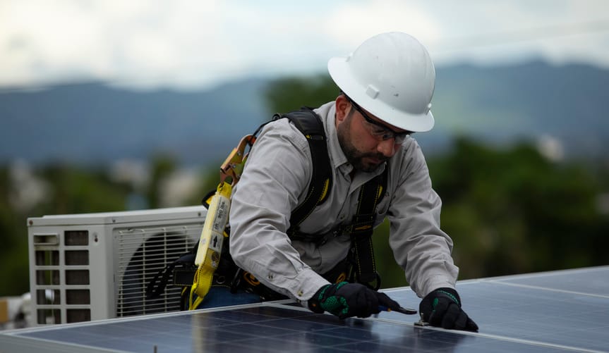A man in a white hard hat installs a solar panel