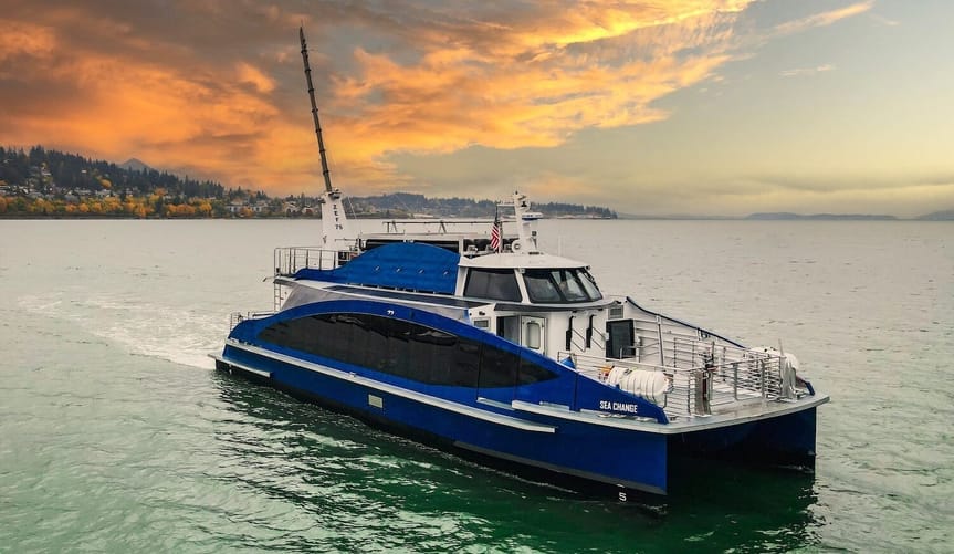 A blue and white catamaran sails over the water during sunset