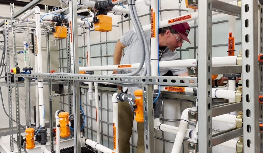 An engineer standing inside an array of tubes and pumps monitors equipment