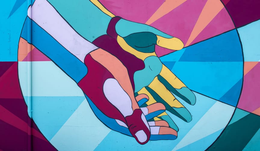 A painted mural depicting two outstretched hands against a colorful geometric backdrop