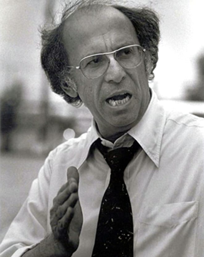 Black and white photo of man with glasses, speaking.