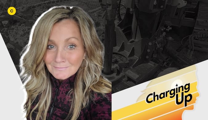 A smiling woman with light skin and long blonde hair wearing a black-and-maroon shirt. A stylized graphic says Charging Up.