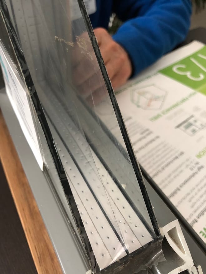 A portable cross-section of a triple-pane window on a table with a person's hand.