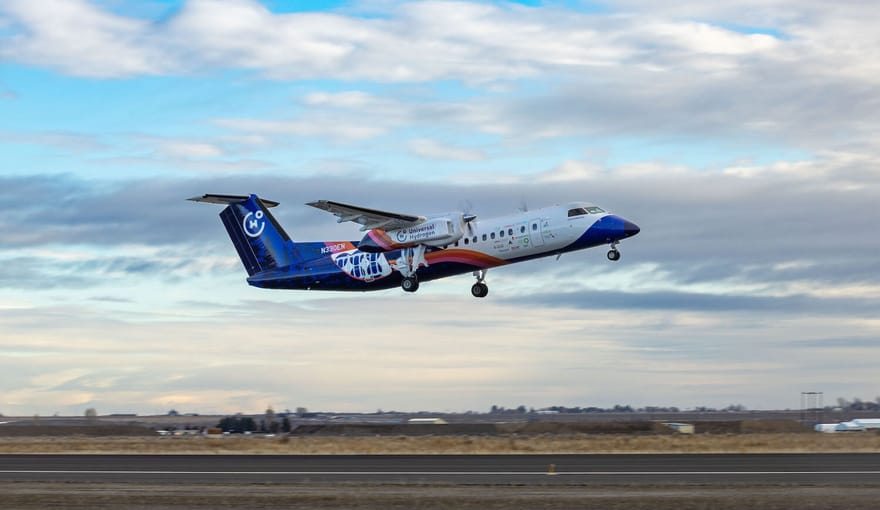 A white-and-blue airplane with twin propellers takes off from an airport landing strip.