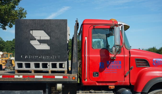 A pile of concrete blocks a sign with CarbonBuilt's logo sit on the flatbed trailer of a big red truck.
