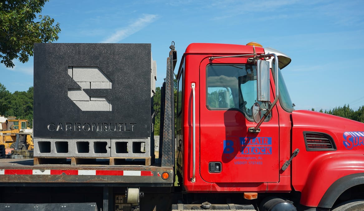 A pile of concrete blocks a sign with CarbonBuilt's logo sit on the flatbed trailer of a big red truck.