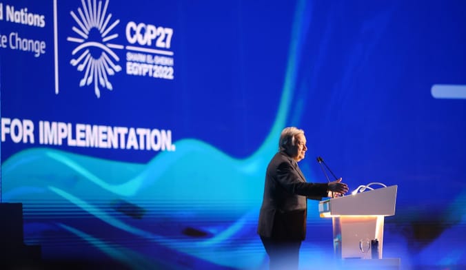 A man wearing a dark suit speaks at a lectern in front of a COP27 sign