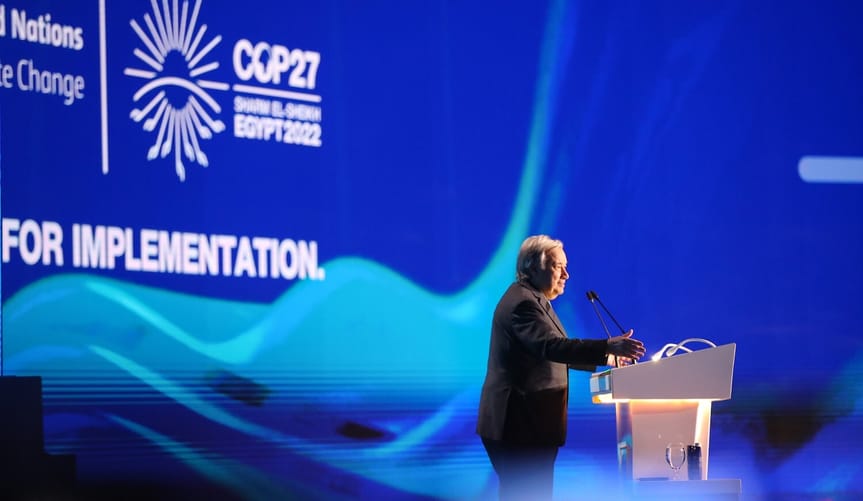 A man wearing a dark suit speaks at a lectern in front of a COP27 sign