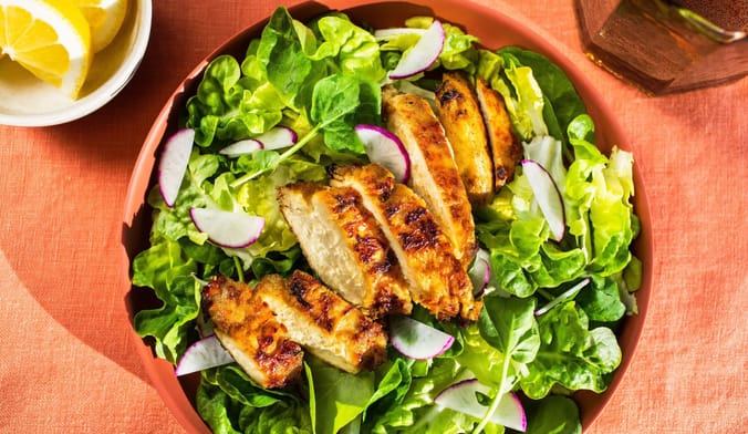 A plate of lettuce and radishes with grilled chicken array in a row in the center