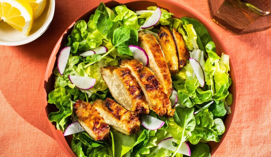 A plate of lettuce and radishes with grilled chicken array in a row in the center