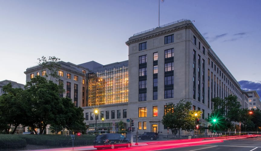 Large corner building at dusk with American flag flying from roof.