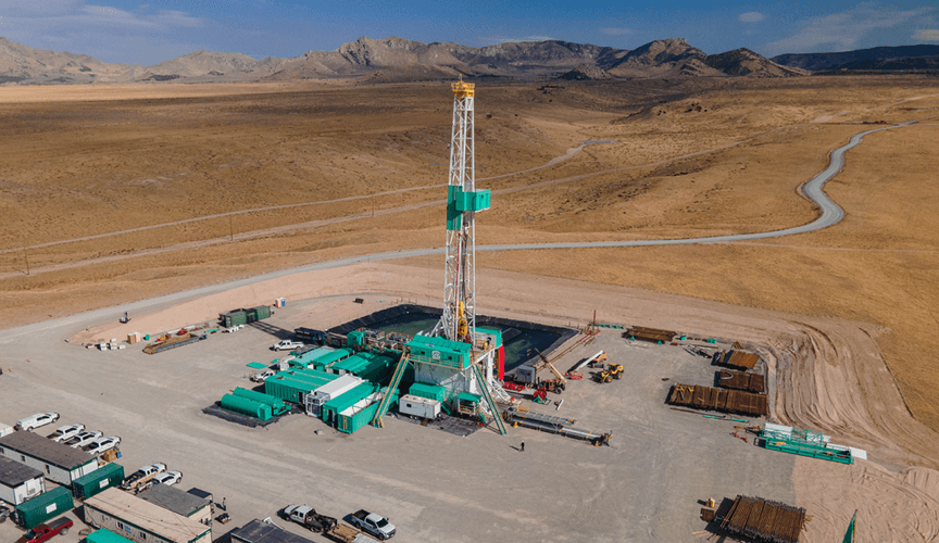 A large industrial site in a desert valley with mountains in the distance. A tall metal tower is seen at center.