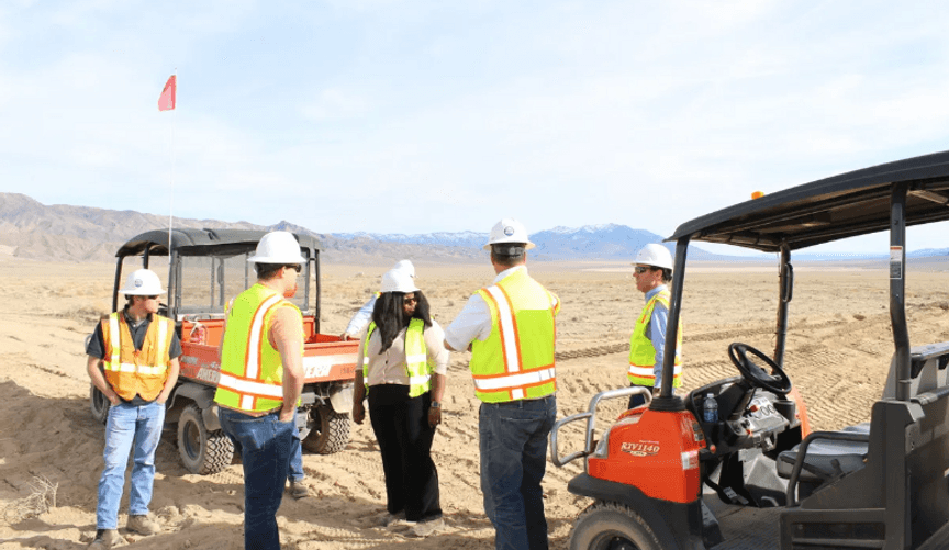 A group of workers in safety gear stand next to vehicles in a vast open space
