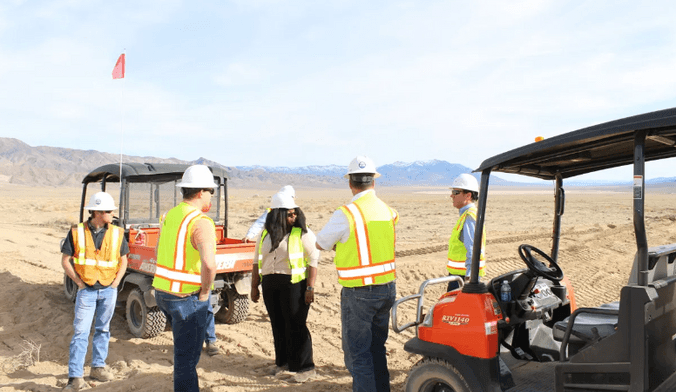 A group of workers in safety gear stand next to vehicles in a vast open space