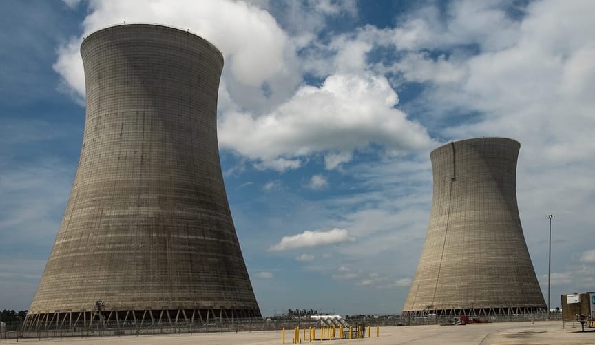 Two concrete cooling towers stand tall against a blue sky with white clouds